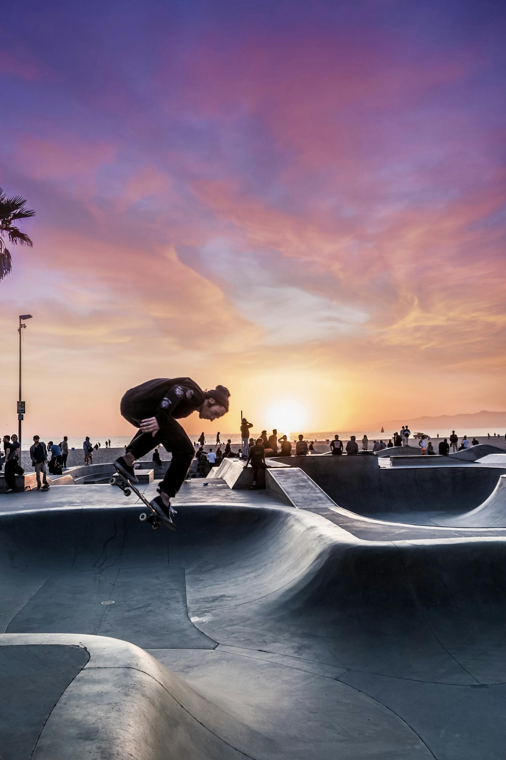 Dynamic shot of a skateboarder in action at Venice Beach Skatepark during sunset.